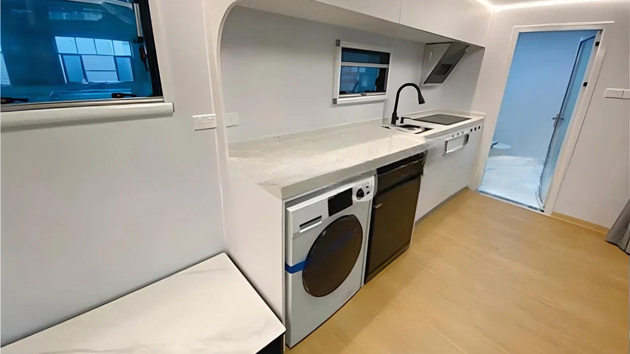 Compact kitchen with washing machine, sink, and window inside AR-3 Extended Apple Cabin living space.