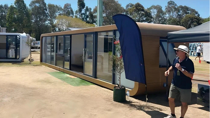 Portable living Ap-3 Extended Apple Cabin on display with a person standing next to one, under a clear blue sky.