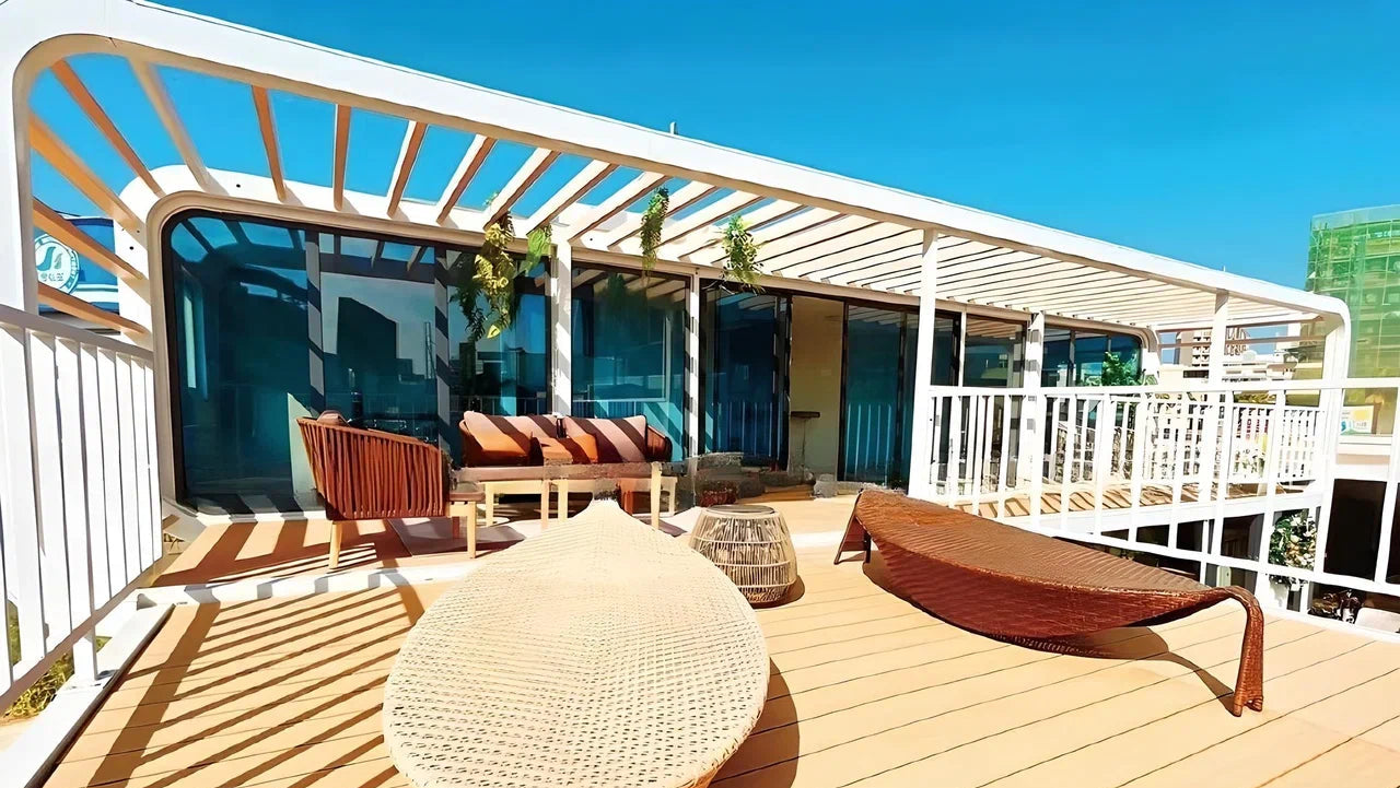 Outdoor deck with wooden furniture and pergola on a sunny day in front of the modular hotel AP-3 Extended apple cabin pod.