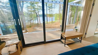 Living room of AP-3 Extended Apple Cabin with large windows overlooking a lake and forest