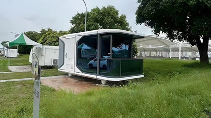Modern modular pod-SX-1 Lite space capsule in a grassy outdoor area with trees and other structures in the background.