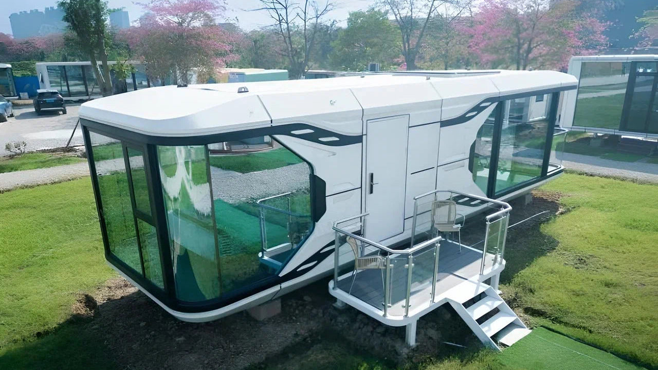 Modern Space Capsule hotel hospitality pod on wheels in a grassy area with trees and buildings in the background