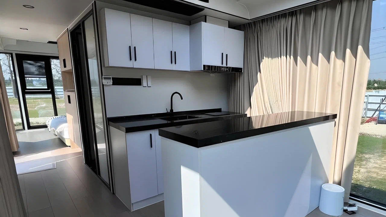 Modern kitchen with white cabinets, black countertops, and a large window inside SX-2 flow space capsule modular pod.