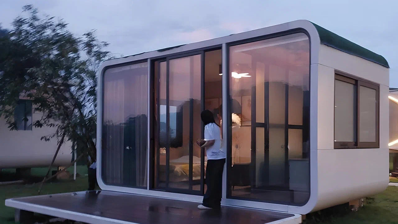 Modern modular Apple Cabin of compact size with a person standing inside, surrounded by greenery.