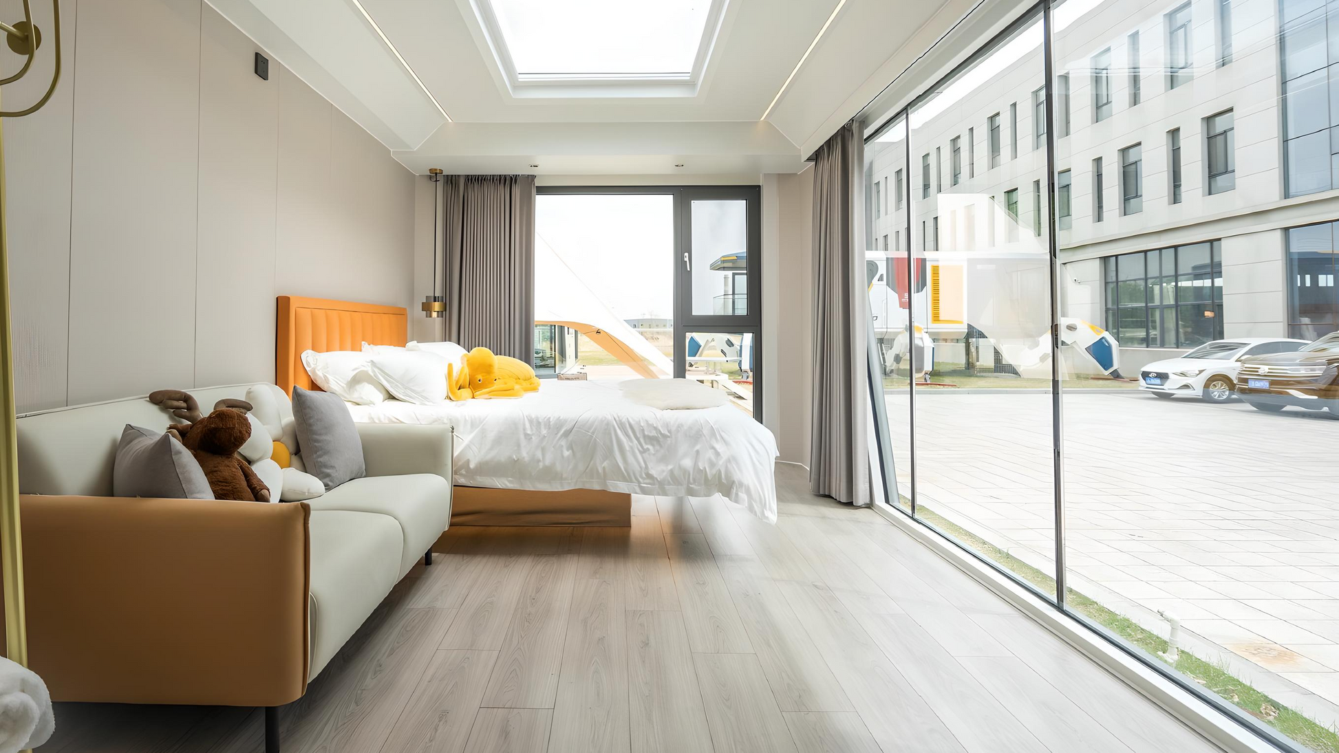 Modern bedroom inside the AP-2 Balanced Apple Cabin modular unit with a large window view of an urban street.