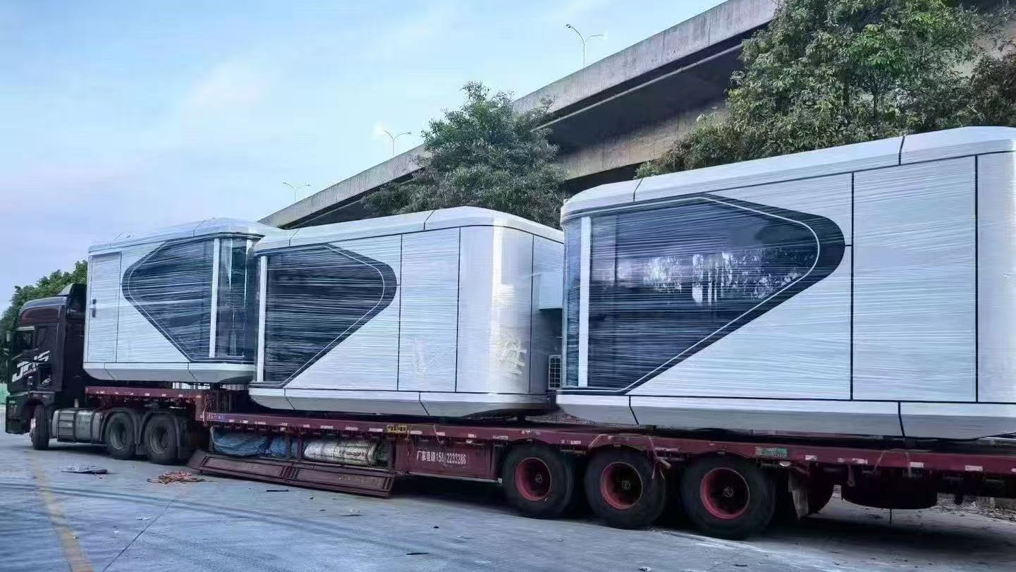 Two futuristic-looking SX-1 Lite space capsule pods on a truck with a building and trees in the background.