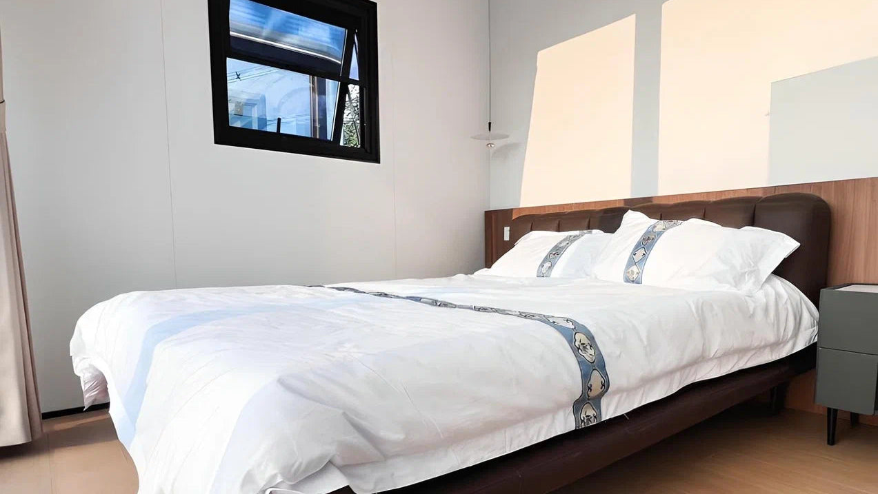 Modern bedroom inside the Apple Cabin unit with a bed, nightstands, and a small window.