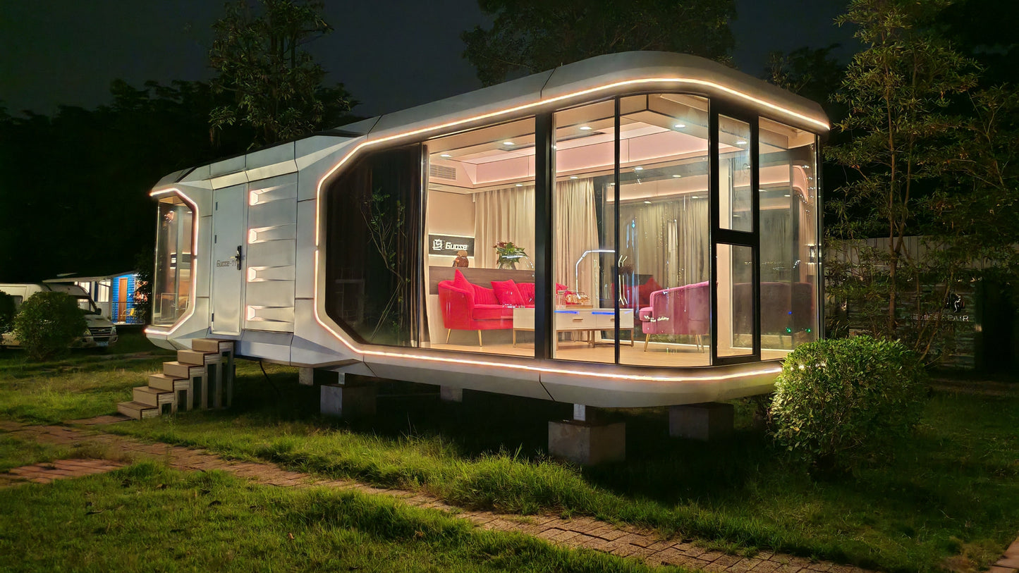 Modern prefabricated SX-2 Flow Space capsule with illuminated interior at night, surrounded by greenery.