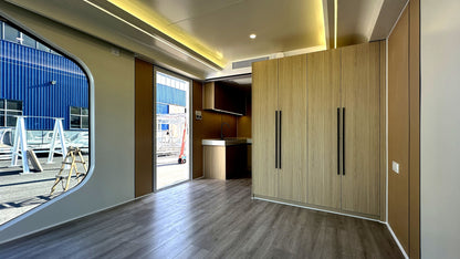 Modern interior of SX-1 Lite Space Capsule with wooden cabinets and a view of a construction site outside.