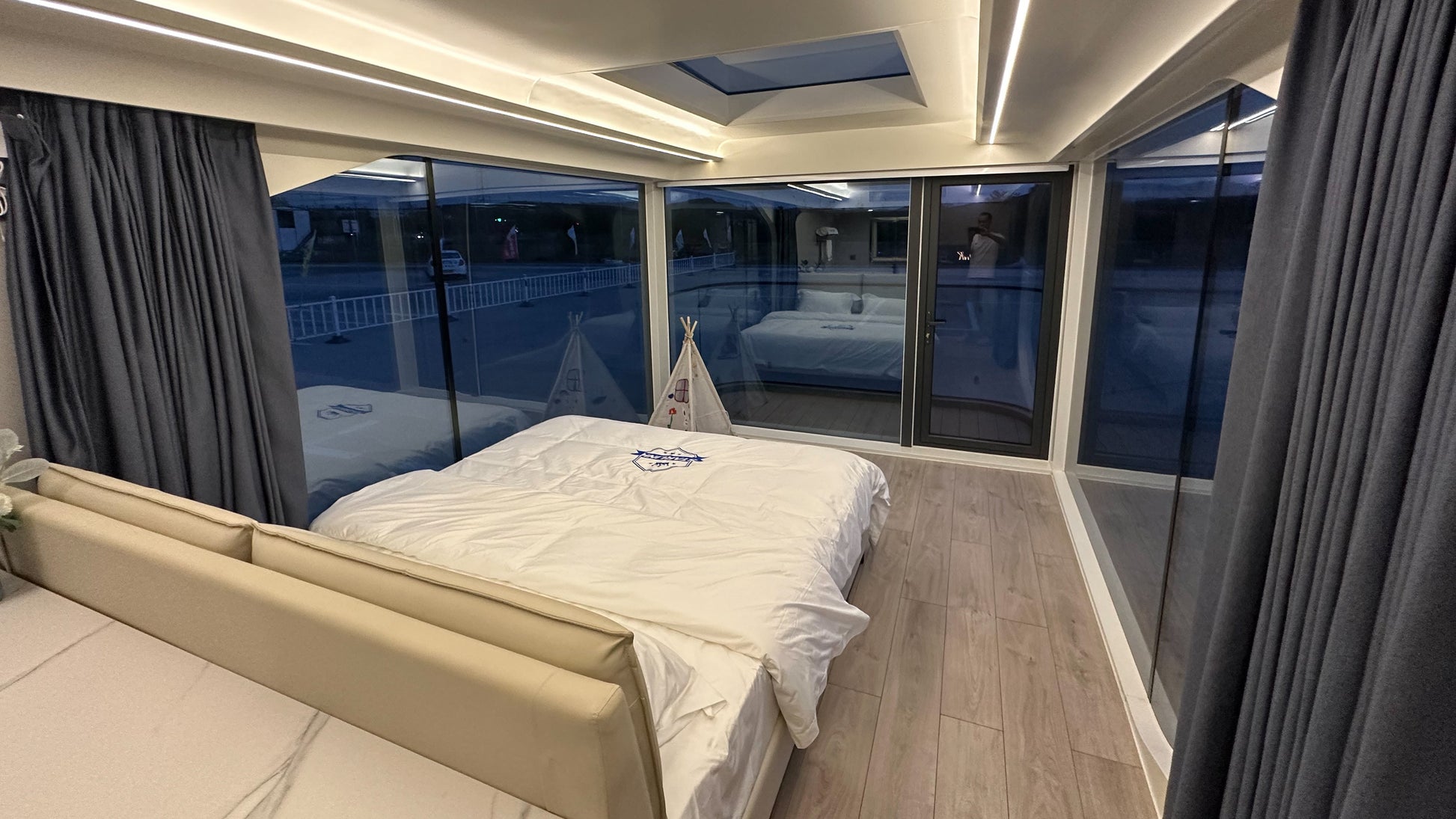 Modern bedroom of SX-1 Lite Space Cabine with large windows, bed, and gray curtains.